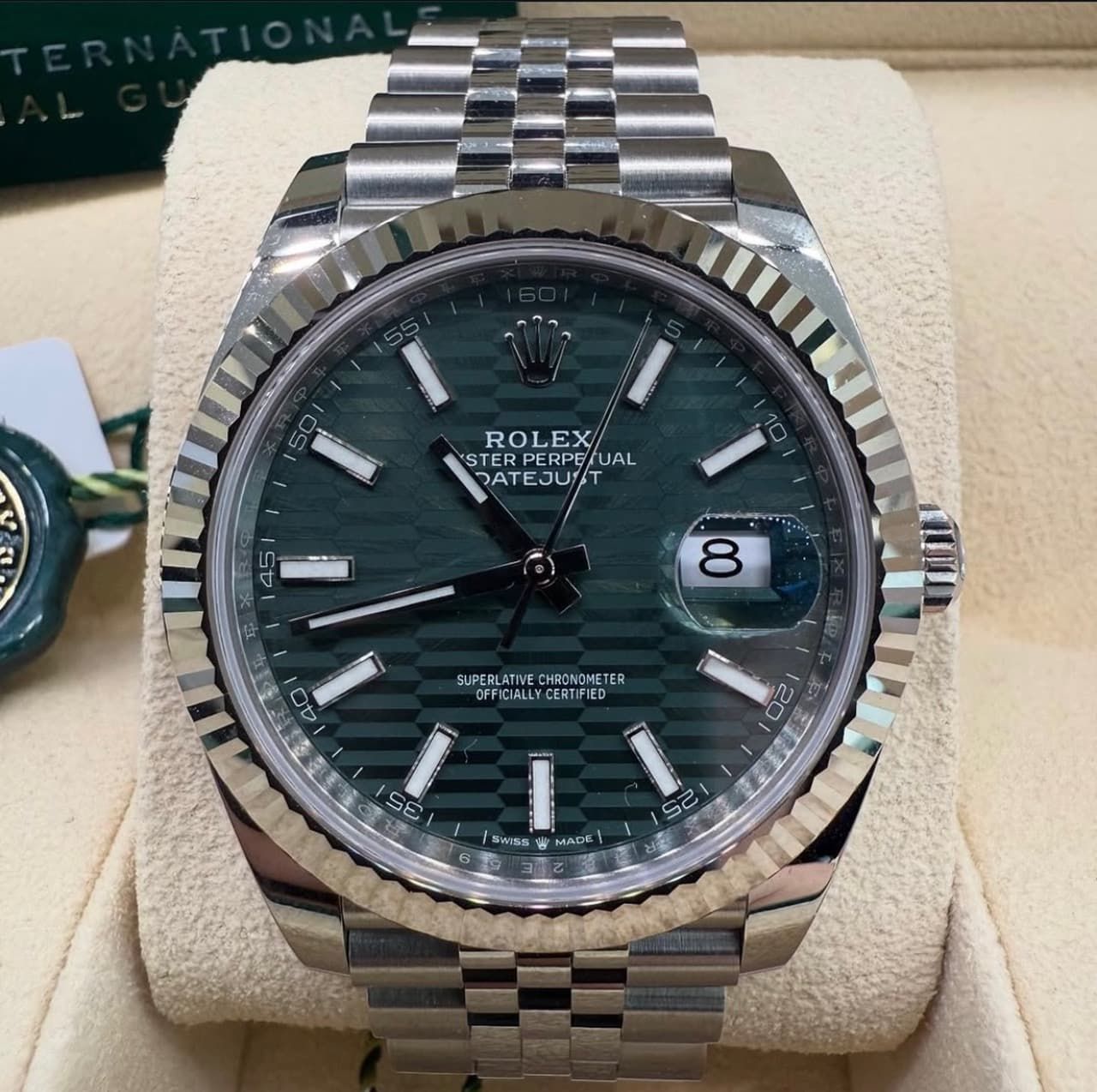 Rolex wristwatch with dark green dial, date window, and silver bracelet on a display cushion