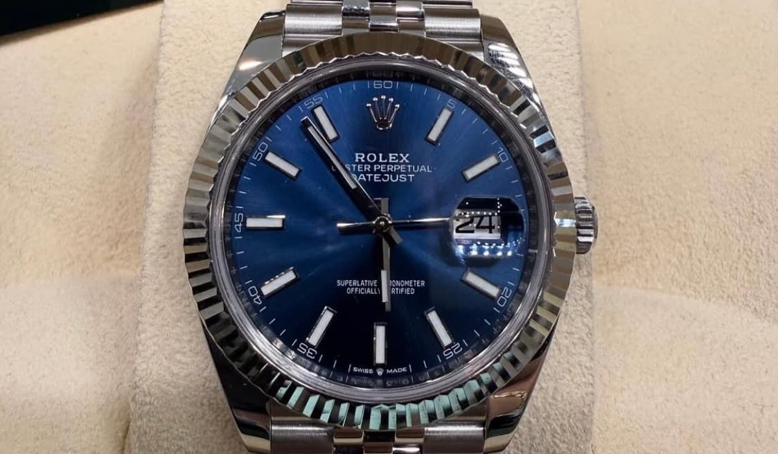 Blue-faced Rolex watch with silver bracelet, shown close-up on a beige background