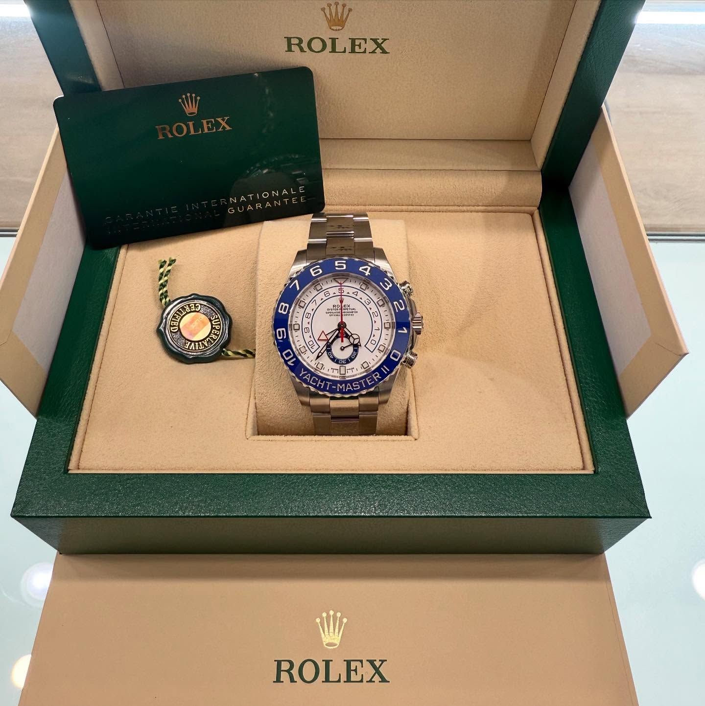 Rolex watch set in green and beige boxes, with a blue bezel and a smaller ring beside it