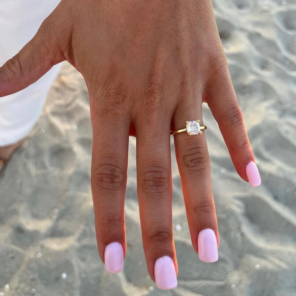 Hand with pink nails and a gold ring over sandy beach background