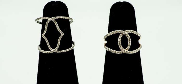 Two silver chain-link bracelets displayed on black stands against a white background