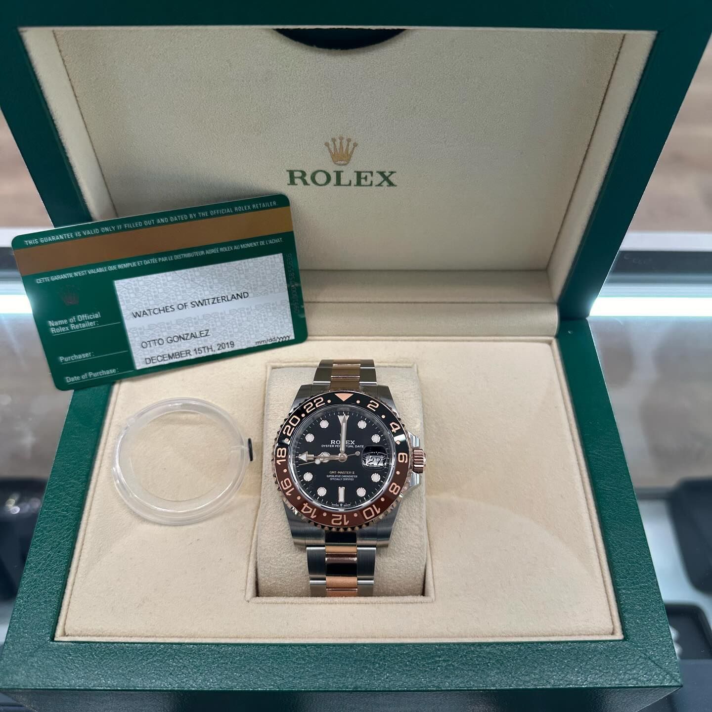 Rolex watch in an open green presentation box with papers and a clear plastic stand