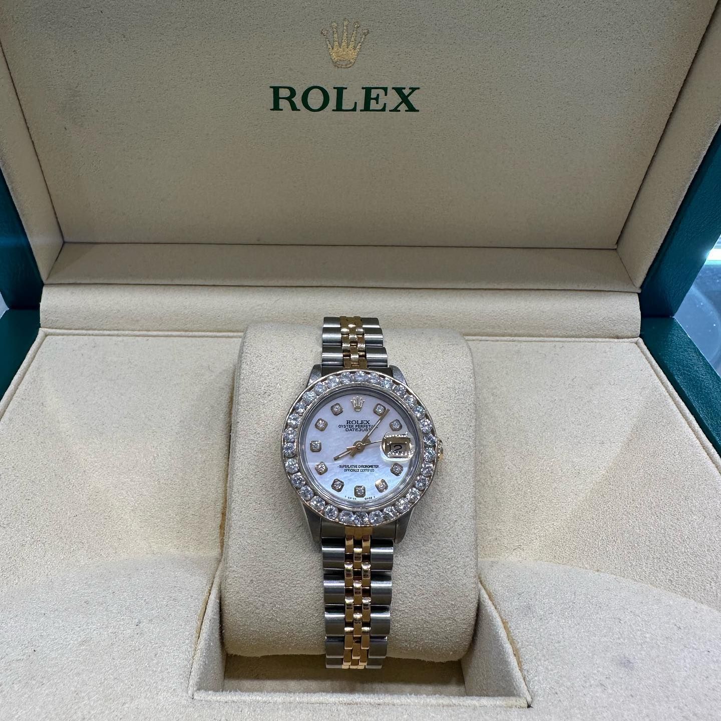 Rolex watch with diamond bezel in a green presentation box with gold accents