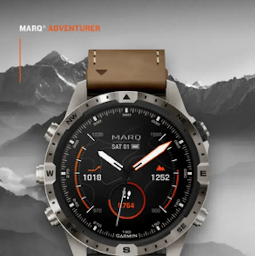 MARQ Adventurer smartwatch with black dial and tan strap against a grayscale mountain backdrop