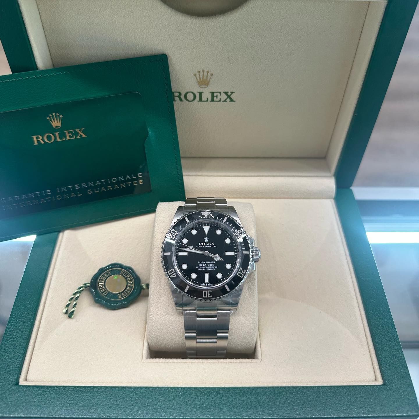 Rolex watch in open green box with booklet and tag, displayed on a cream cushion