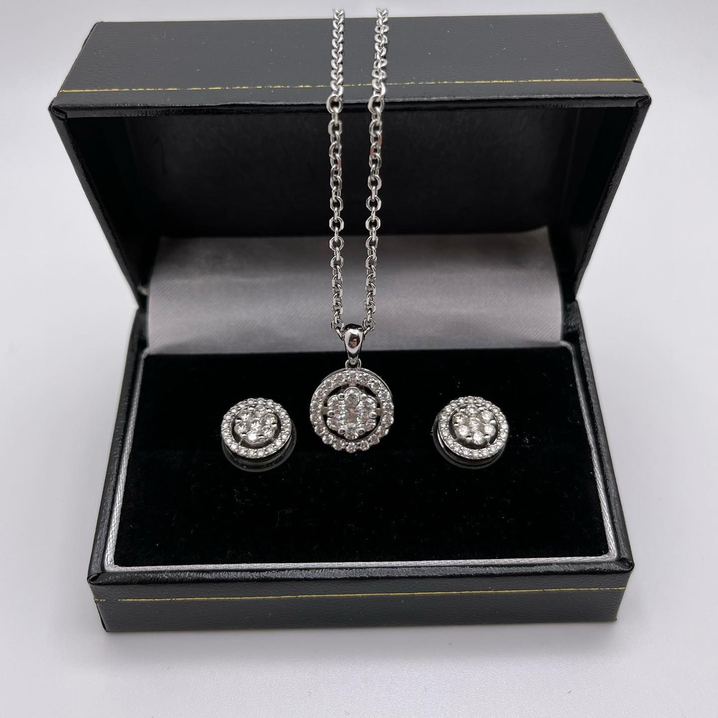 Open black jewelry box with silver necklace and matching earrings on black velvet