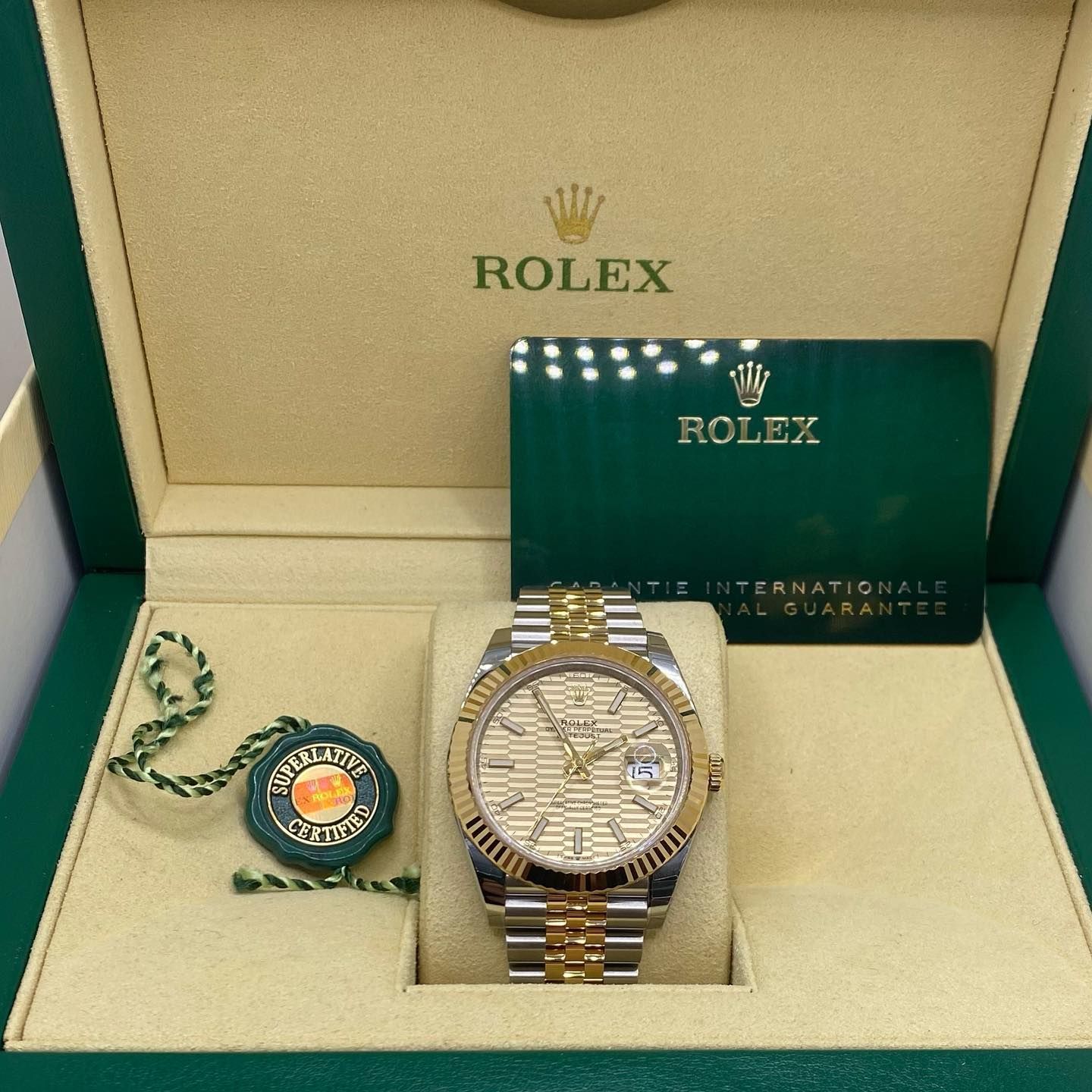 Rolex watch in a green presentation box with warranty card and tag, gold and silver bracelet, white dial