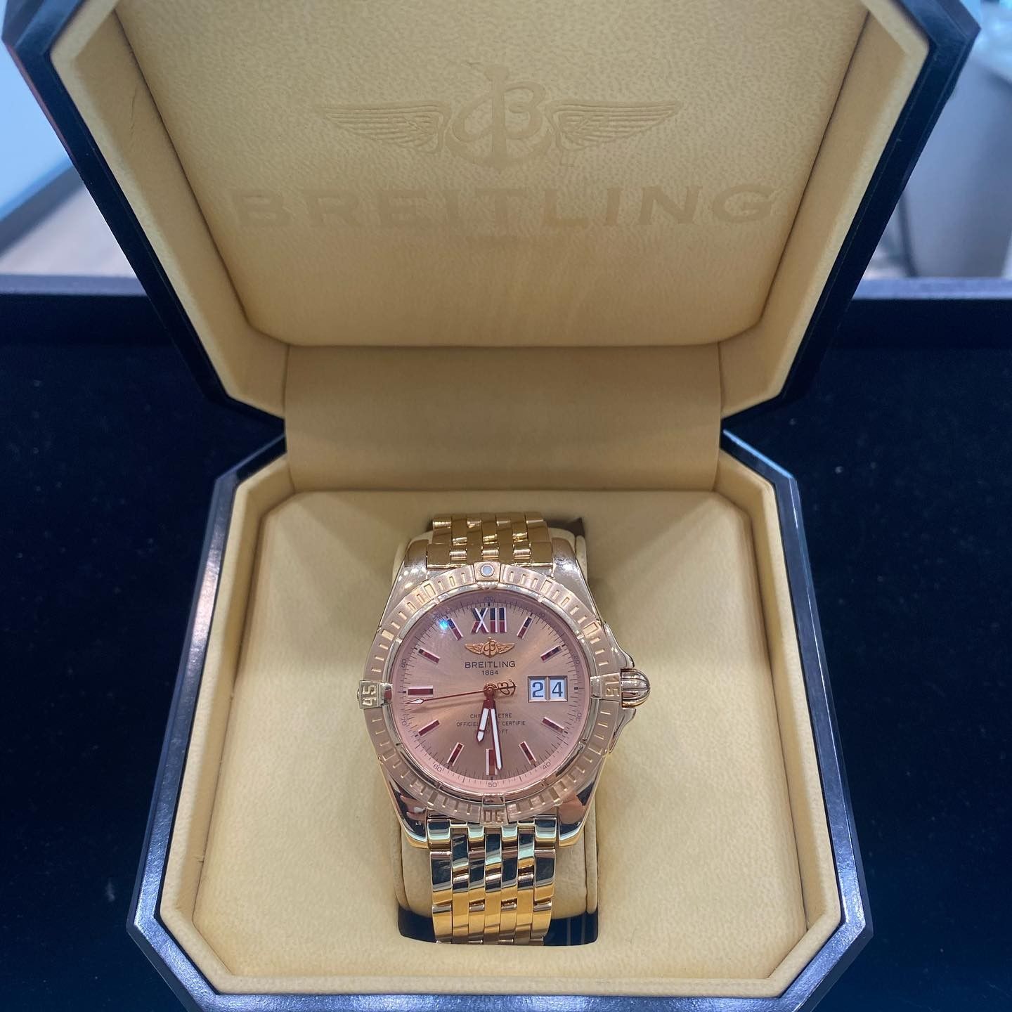 Gold wristwatch with a pink dial displayed in a cream presentation box