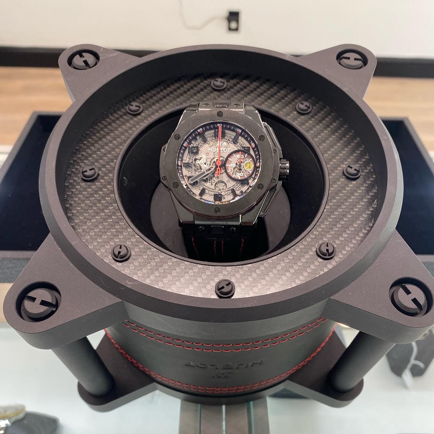 Luxury watch on a black display stand inside a circular case, viewed from above.
