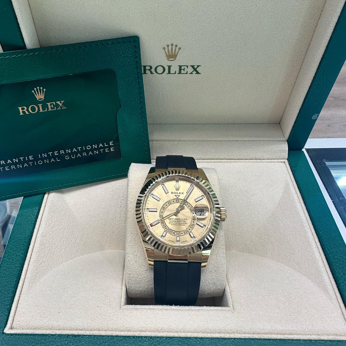 Rolex watch in an open presentation box with a green guarantee booklet, cream dial and dark strap