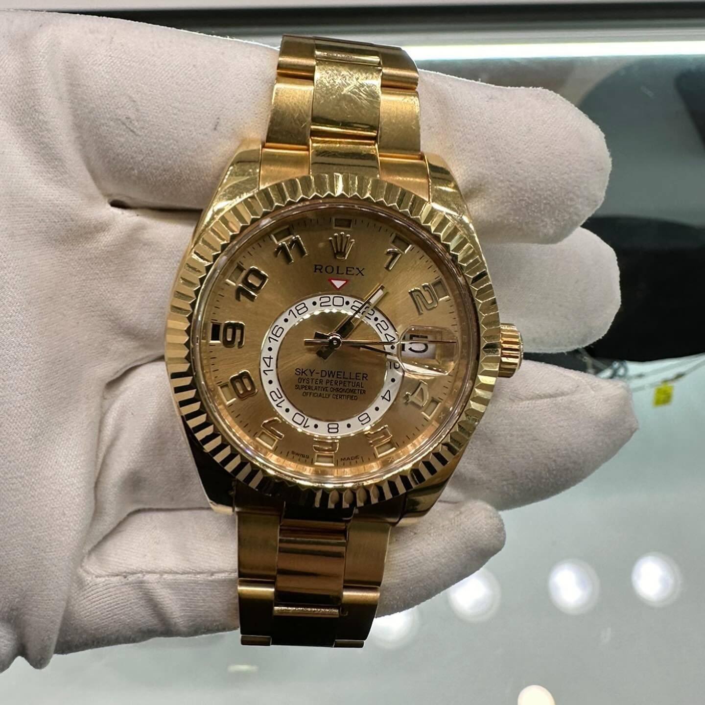 Gold Rolex wristwatch with Roman numerals, held in a white-gloved hand