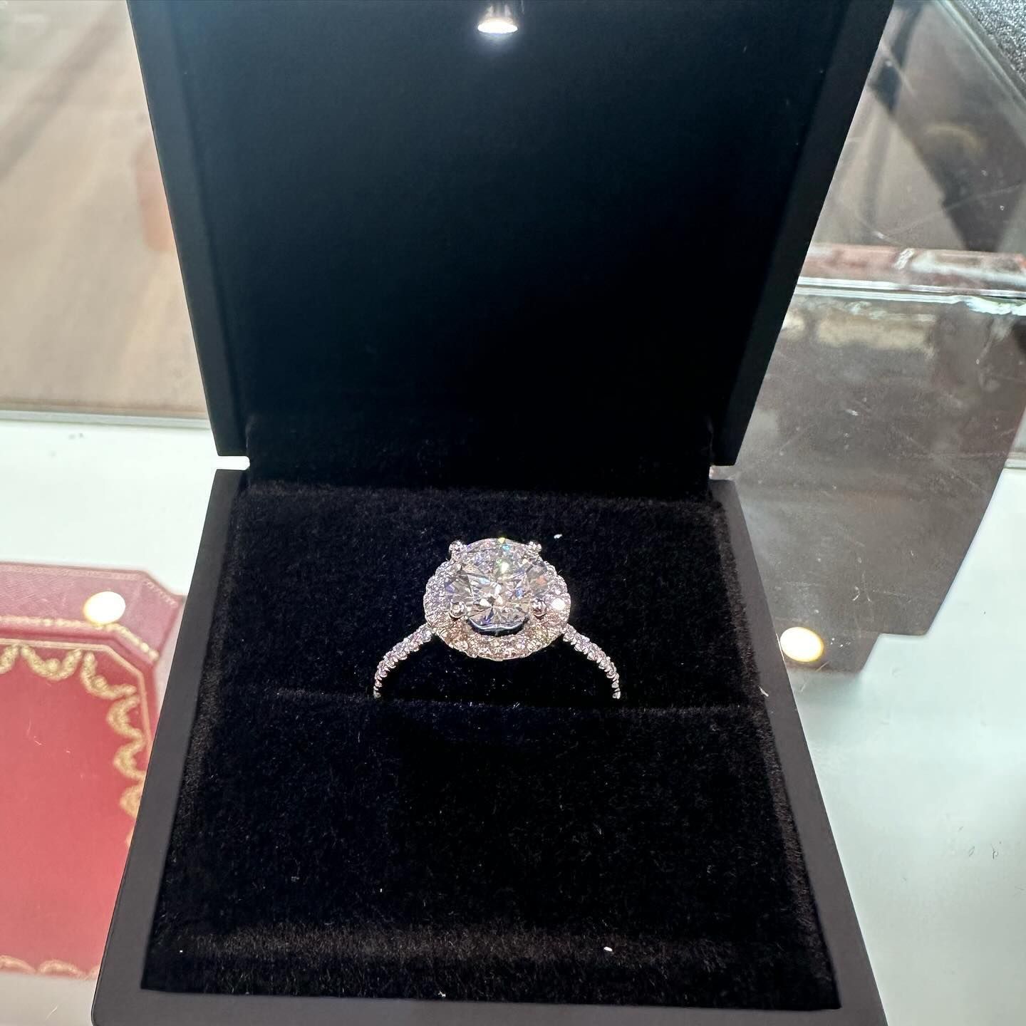 Diamond ring in an open black velvet jewelry box on a glass display table.