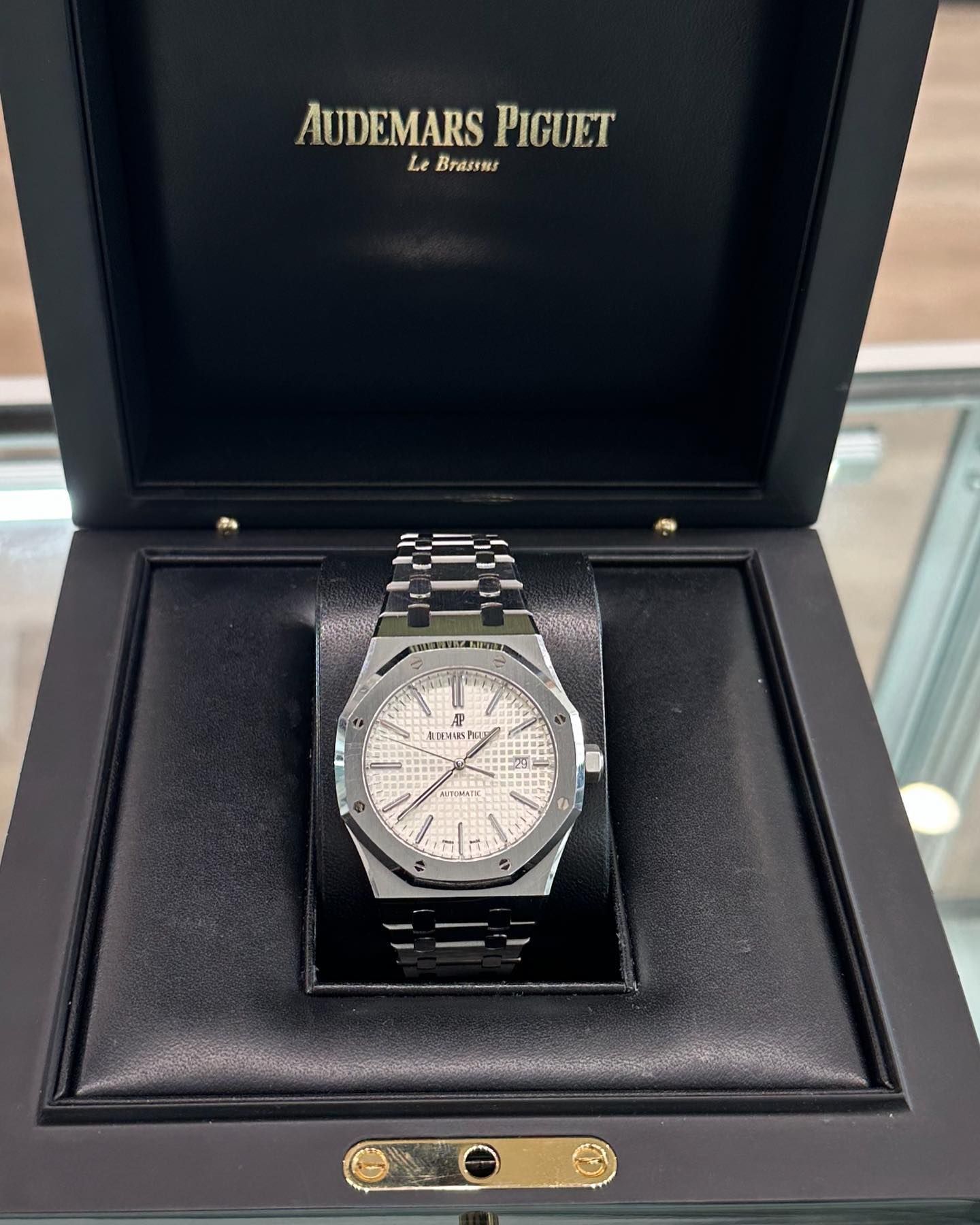 A silver Audemars Piguet watch in a black presentation box, with lid open.