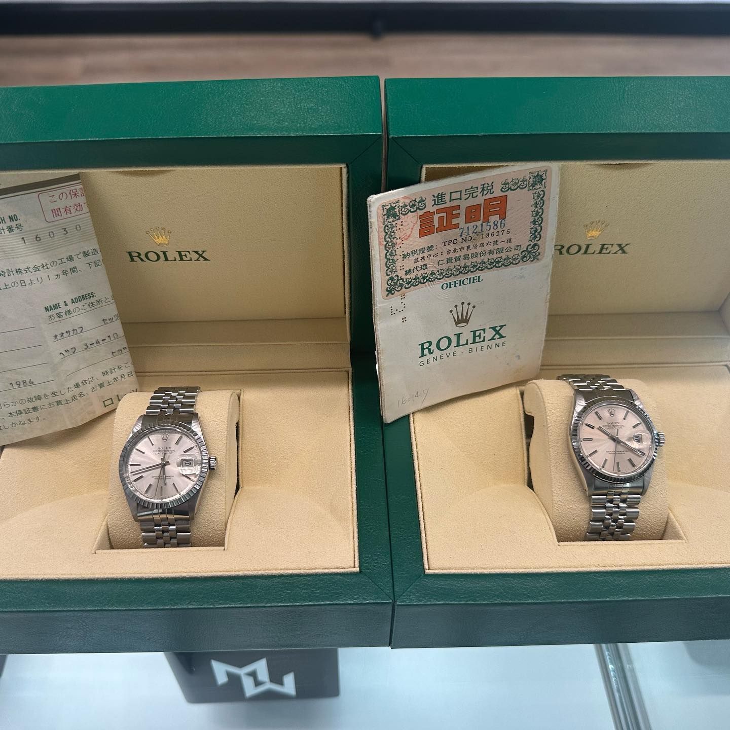 Two Rolex watches in green boxes on display, with warranty cards beside them.