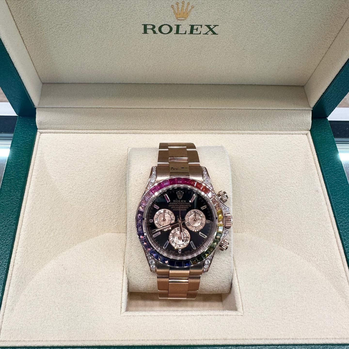 Rolex wristwatch with rose-gold band and gemstone bezel displayed in an open presentation box