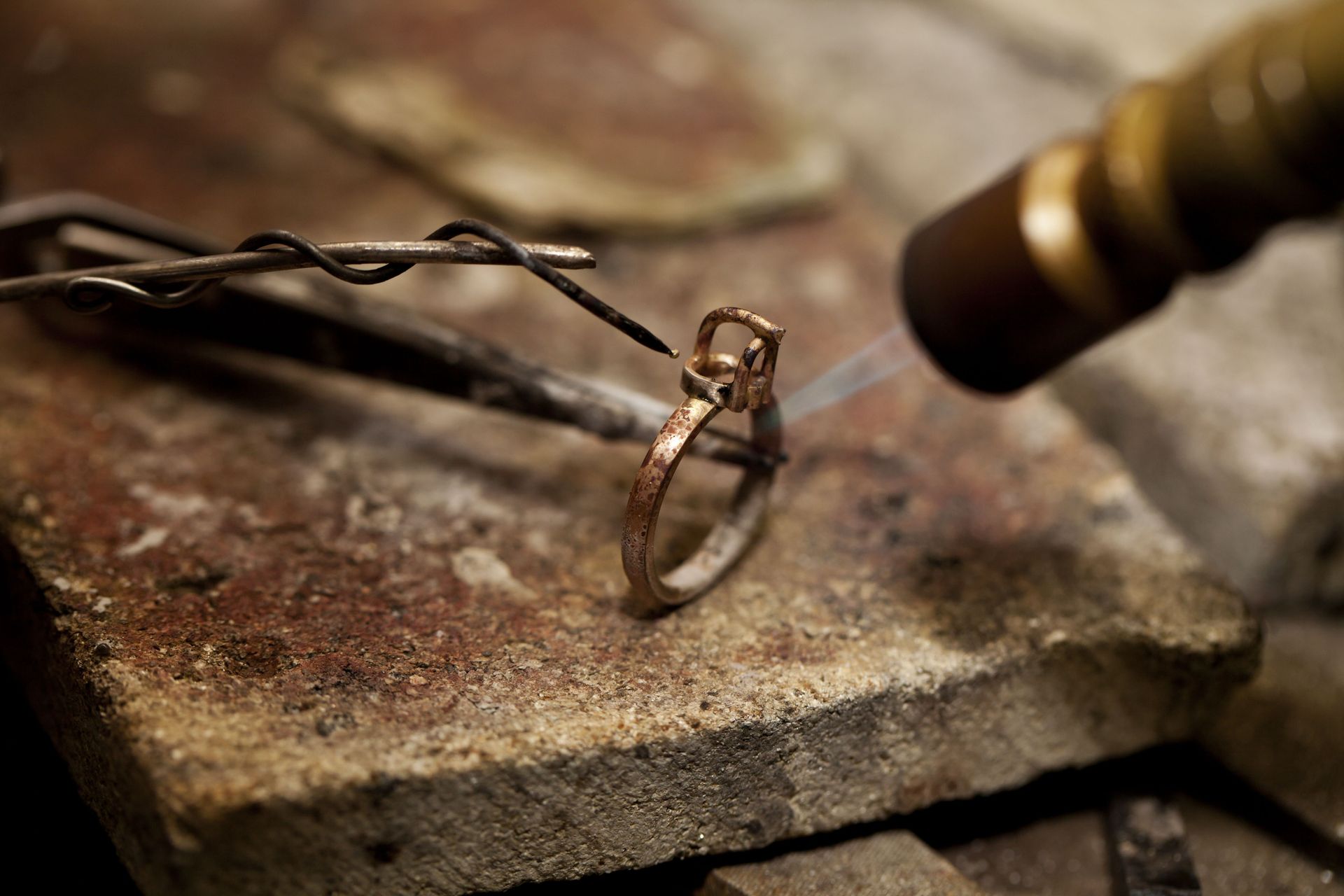 Close-up of a ring being crafted with pliers on a worn workbench, with twisted metal wires nearby