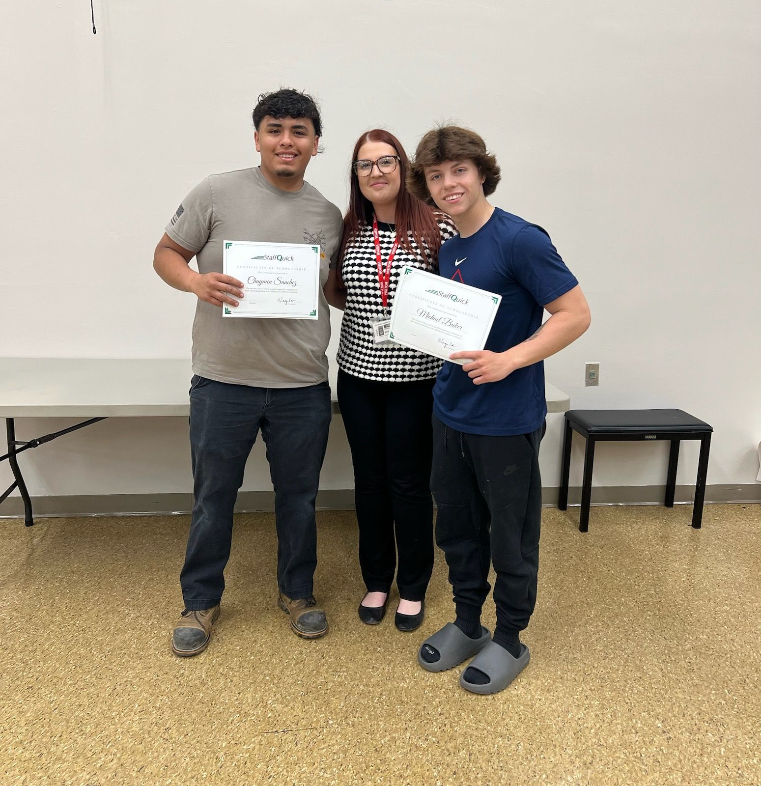Three people with certificates pose indoors. Two young men stand on either side of a woman. All smile.