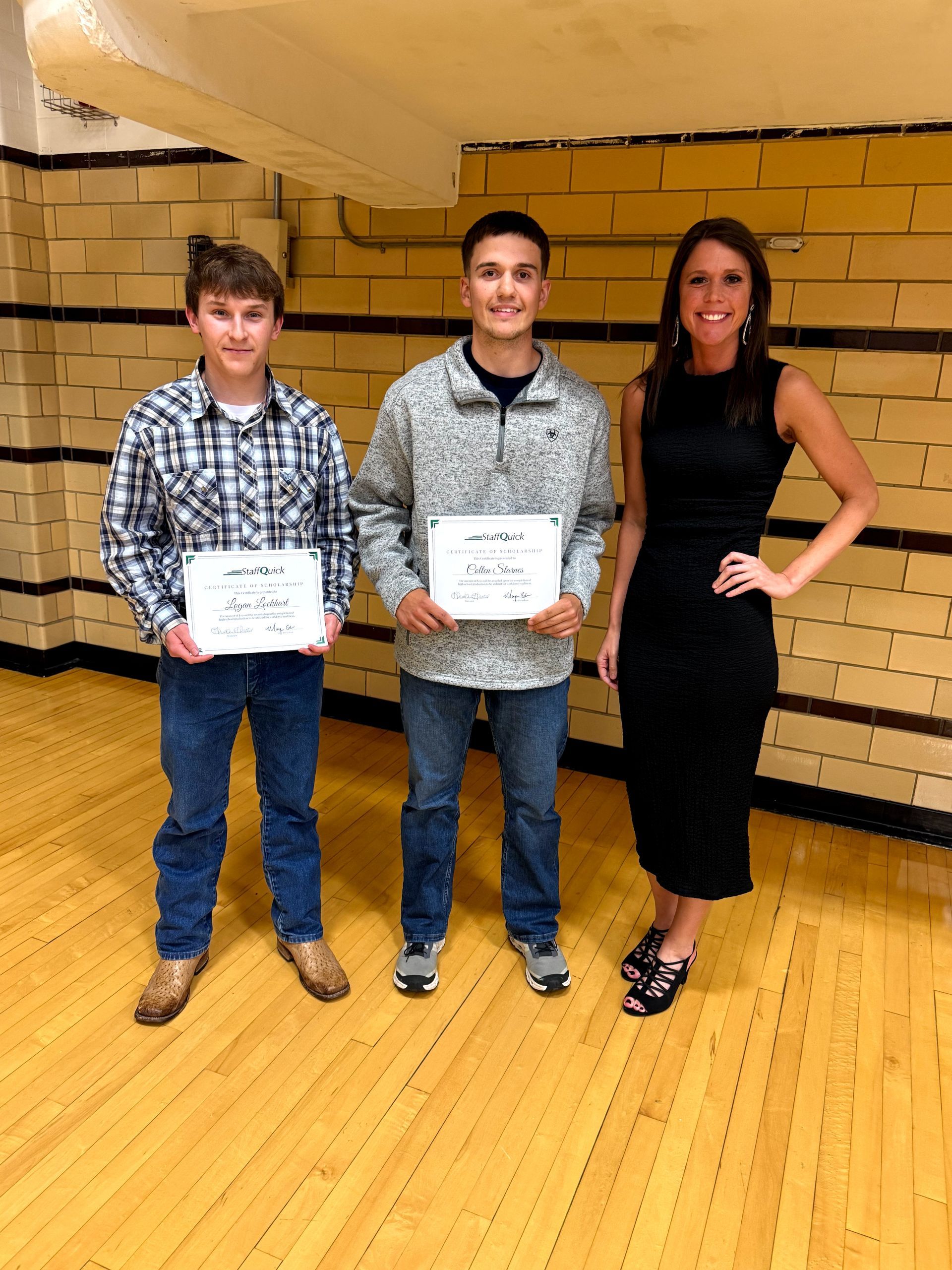 Two boys and a woman holding certificates; standing on a wooden floor near a wall with painted vertical stripes.