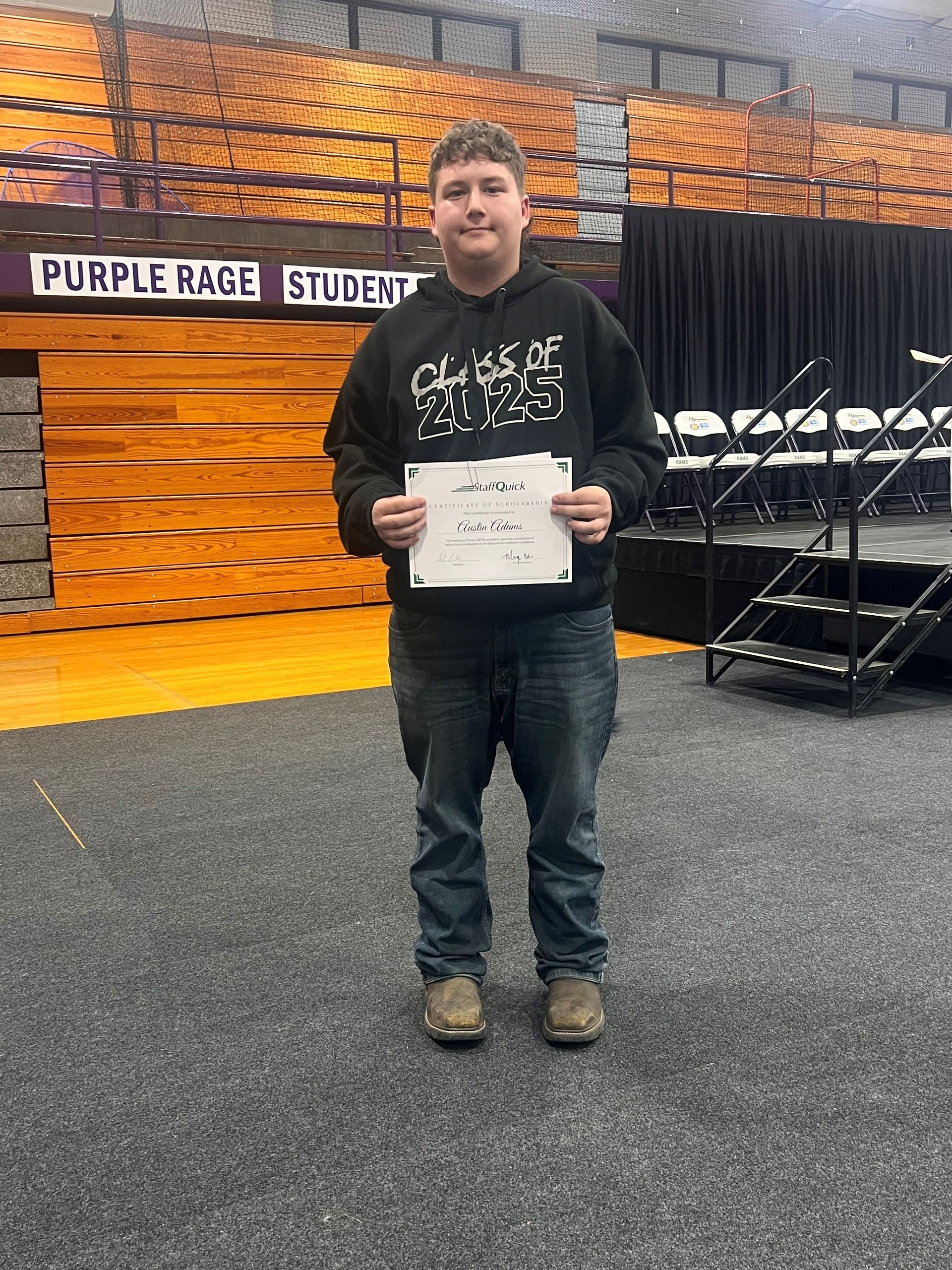Teenager in black hoodie and jeans holding a paper, standing on a stage.