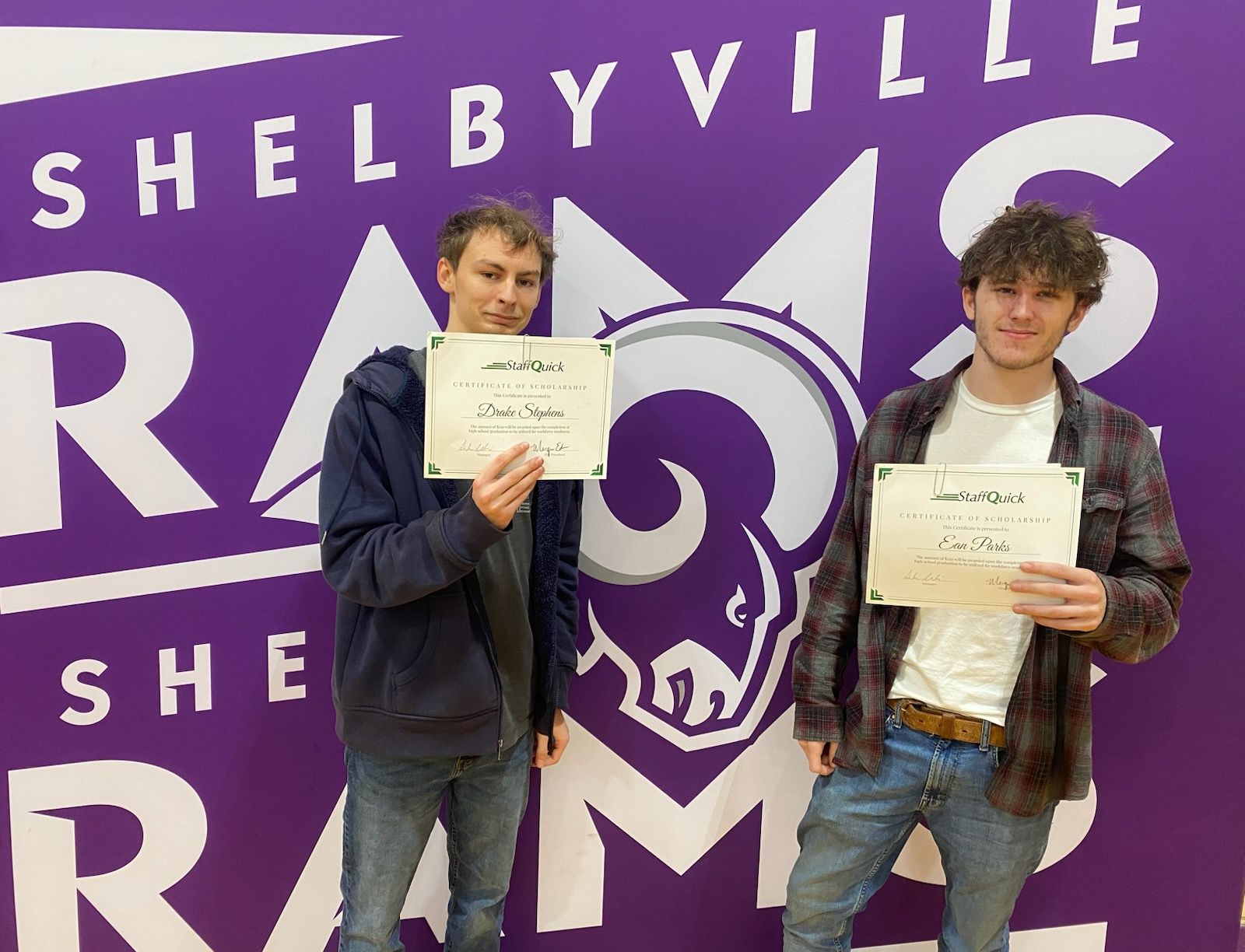 Two young men with certificates stand in front of a purple