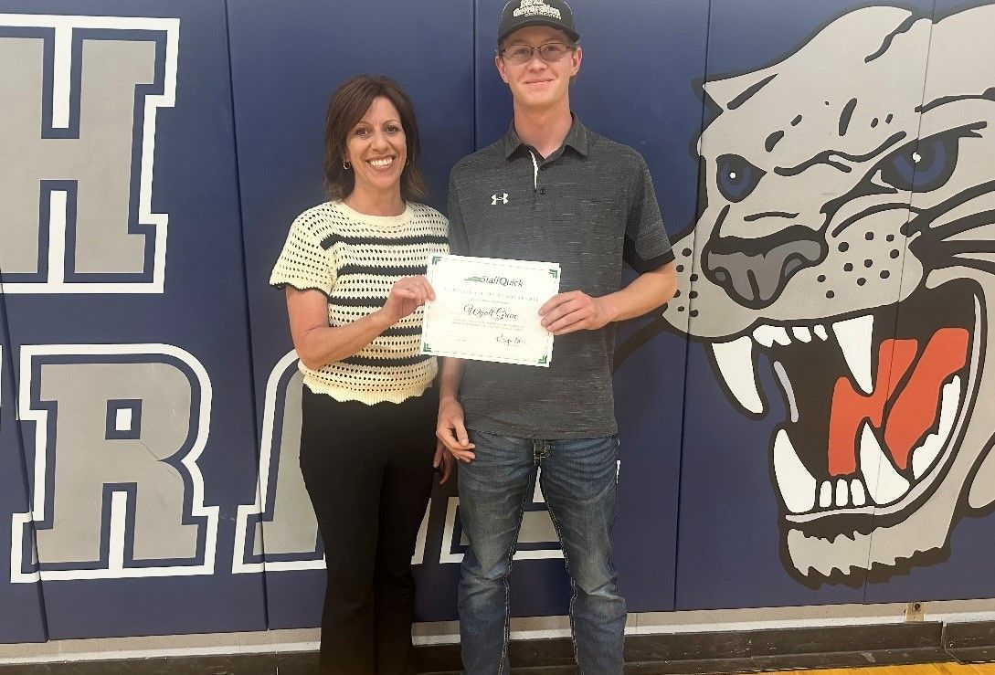 Woman and young man stand near a panther logo, holding a signed paper.