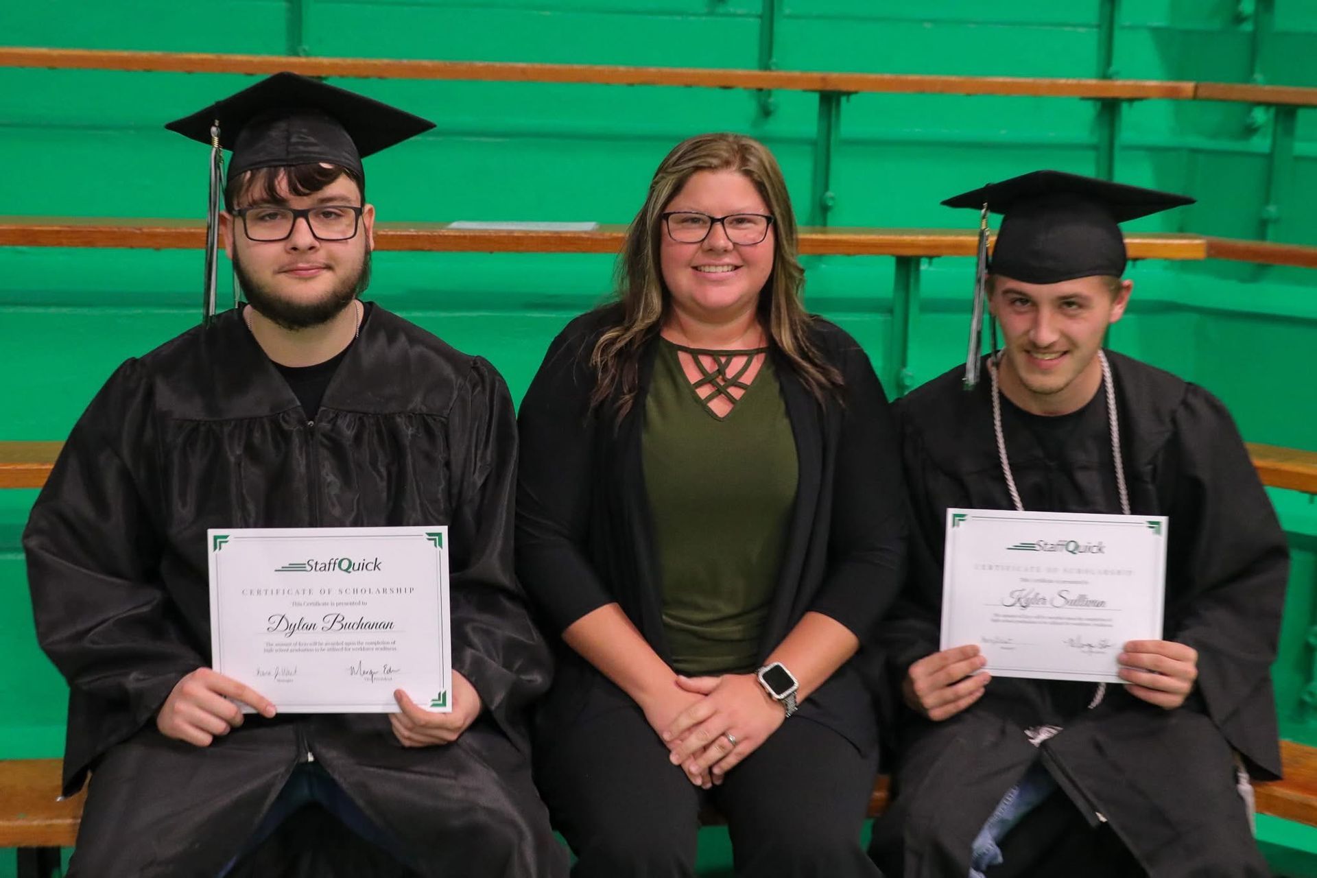 Three people in graduation attire, smiling. A woman in the center, two men holding diplomas. Green background.