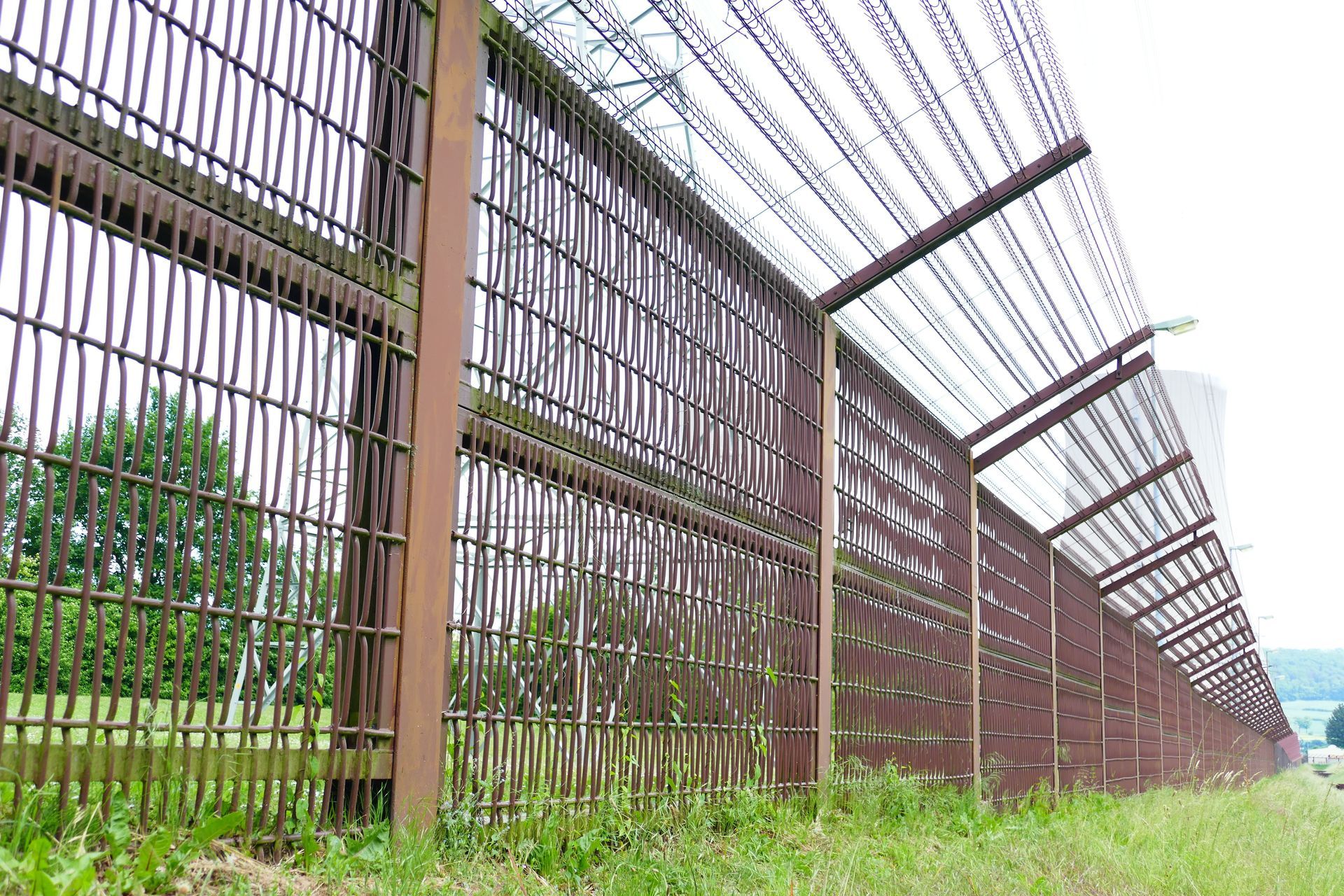 Long, rusty metal fence topped with barbed wire, set in grass.