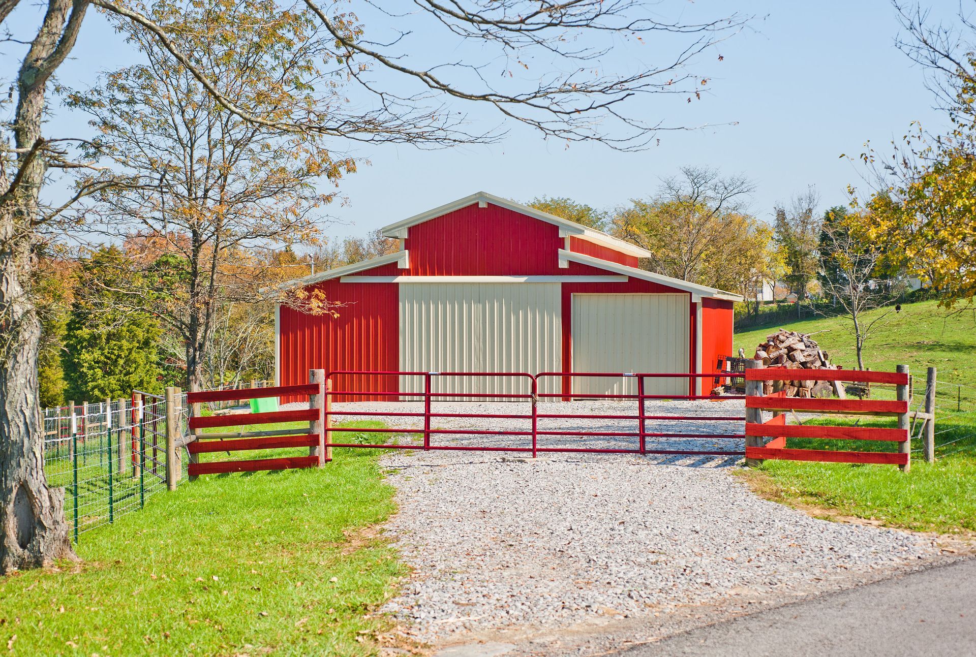 Red barn with white doors, gravel driveway, and red gate on a sunny day.