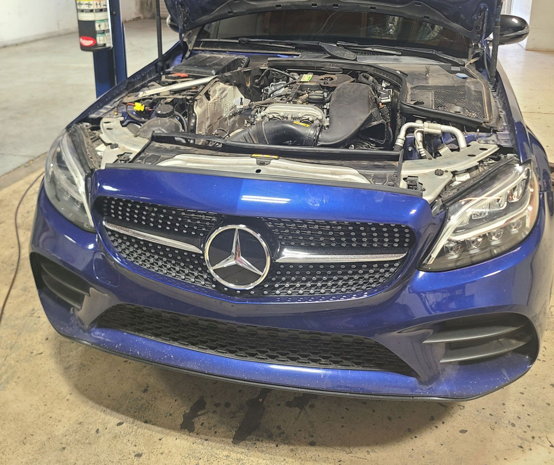 A blue Mercedes with the hood up in a garage