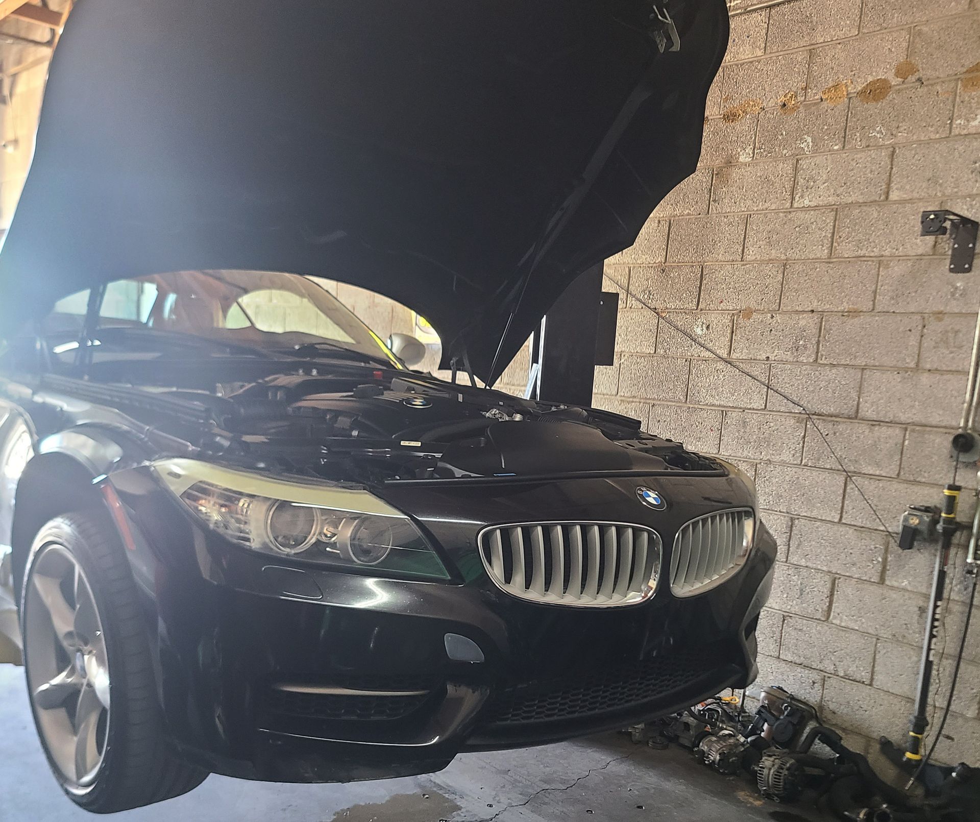 A black BMW car with the hood up is parked in a garage
