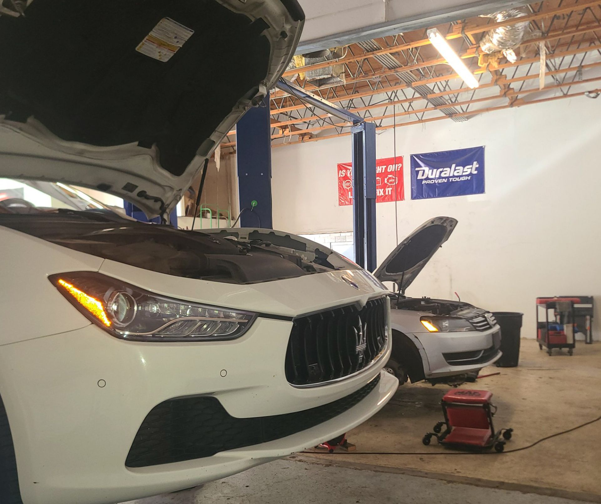 A white Maserati car with the hood up in a garage
