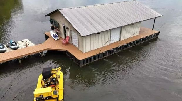 A floating house on water with a dock and a yellow boat nearby.