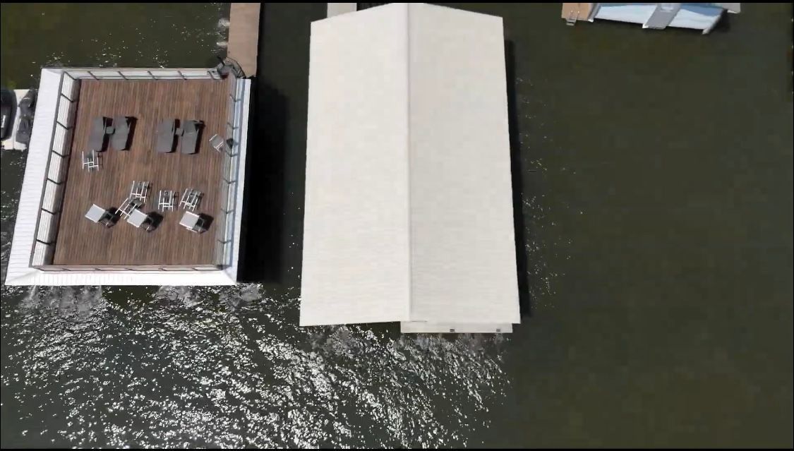 Aerial view of a dock with a covered structure and a small outdoor seating area beside dark water.