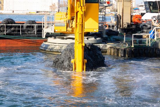 Yellow dredging machine stirring water at a harbor dock