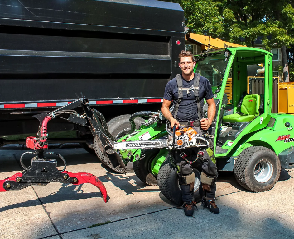 A man is standing in front of a green truck holding a chainsaw.