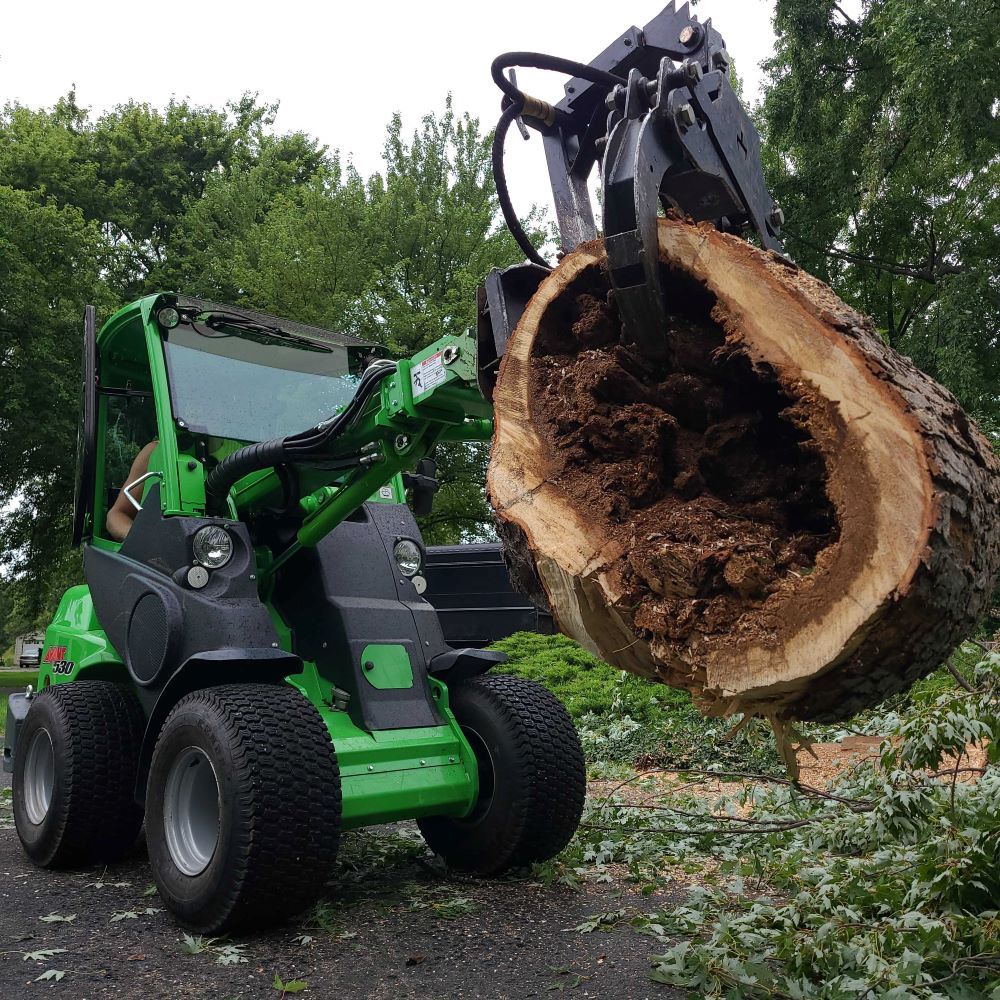 A green and black tractor is carrying a large tree stump.