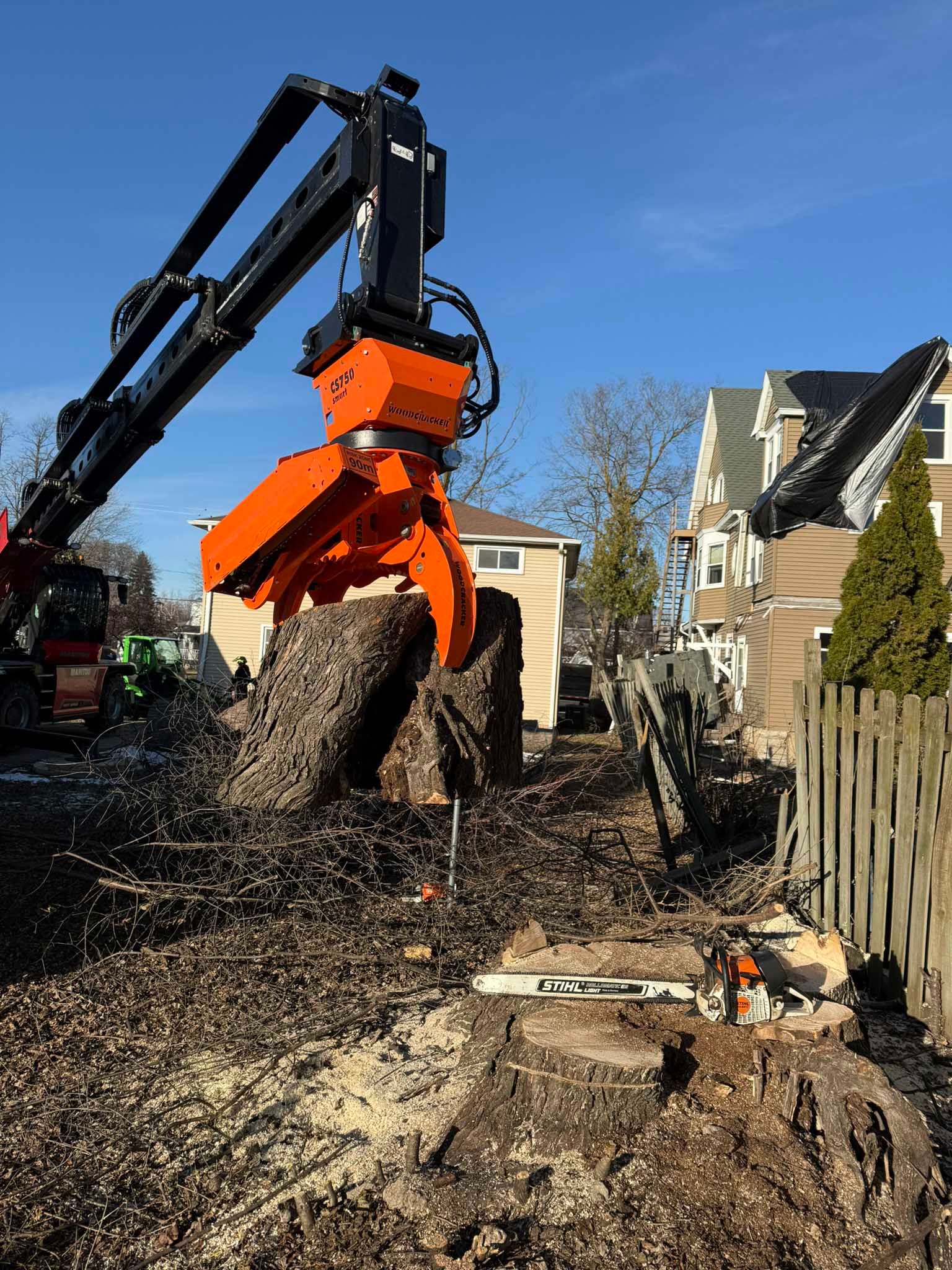 A crane is cutting down a tree in front of a house.