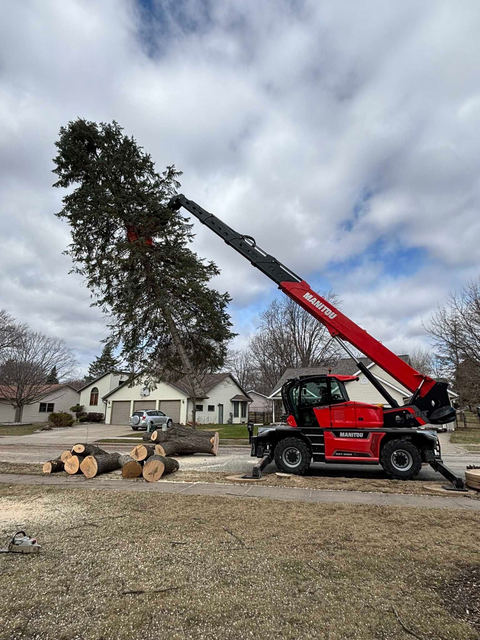 A red crane is lifting a tree in a yard.