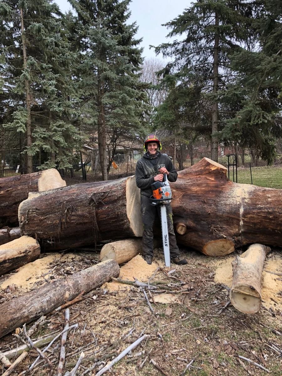 A man is standing next to a large log with a chainsaw.