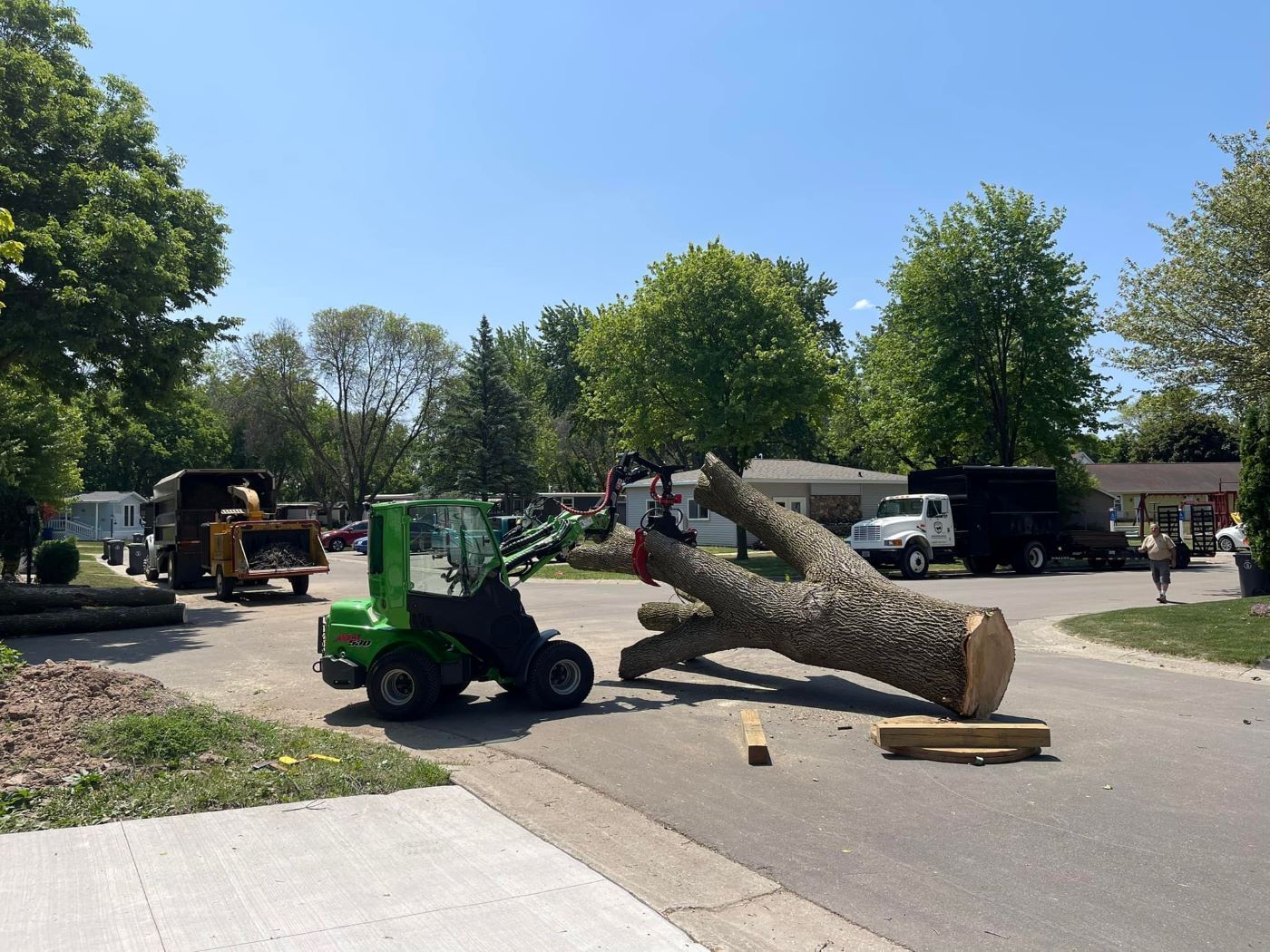 A large tree trunk is sitting on the side of the road next to a forklift.