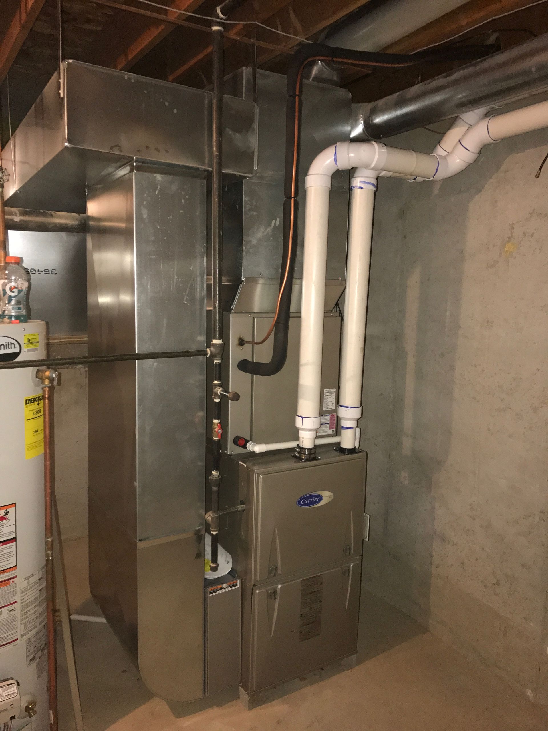 A stainless steel furnace is sitting in a basement next to a water heater.