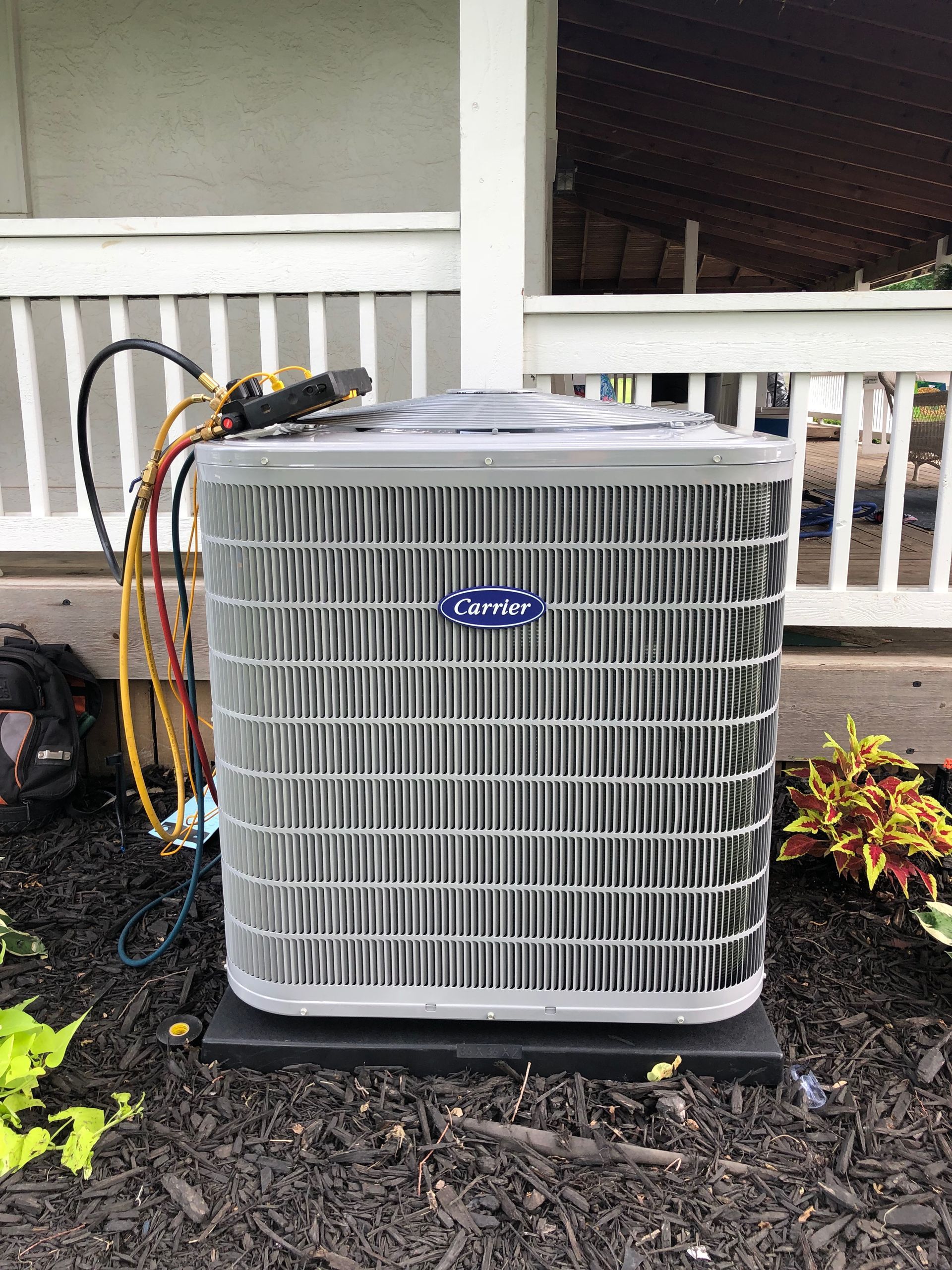 A carrier air conditioner is sitting on the ground next to a porch.