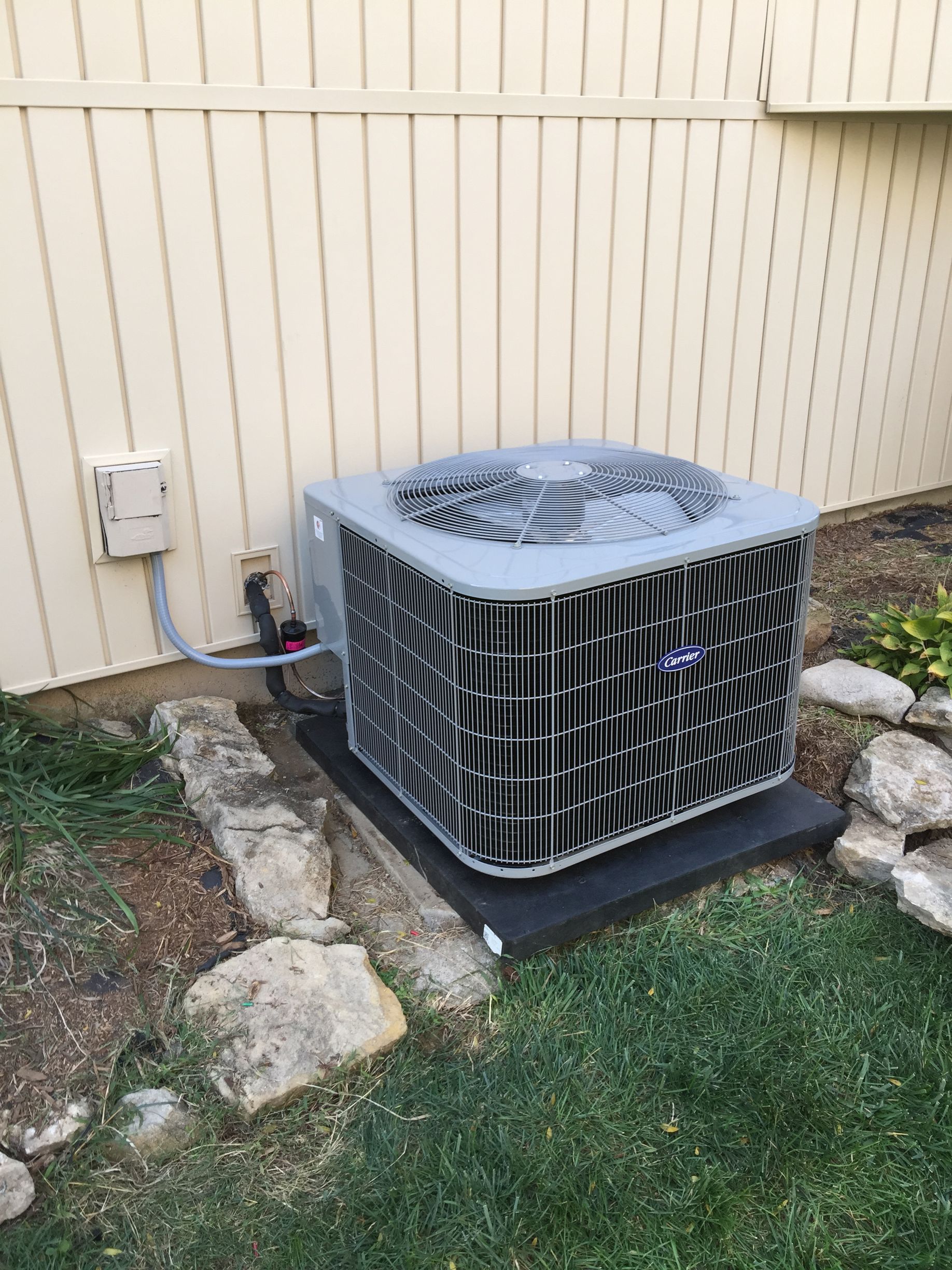An air conditioner is sitting outside of a house next to a fence.