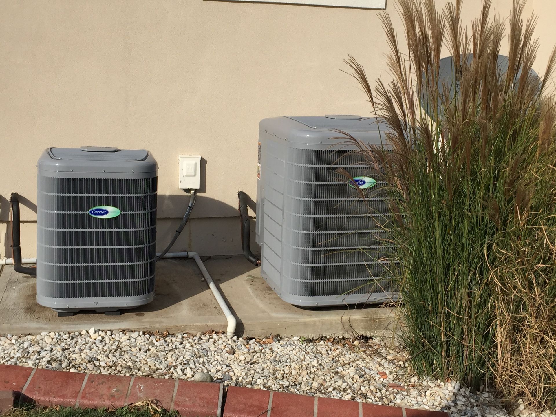 Two carrier air conditioners are sitting outside of a house