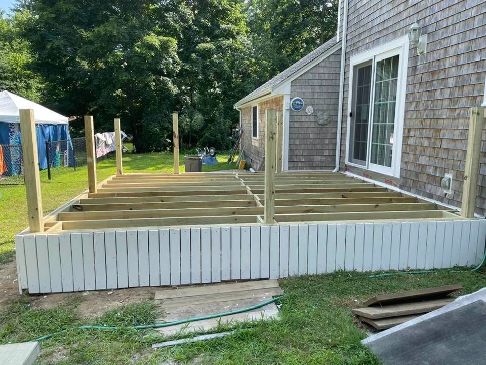Partially constructed deck with white siding and vertical posts; house in background.