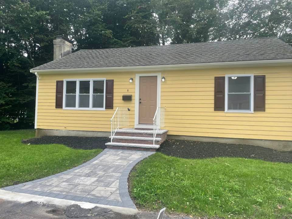 Yellow house with a stone walkway, brown shutters, and a front door.