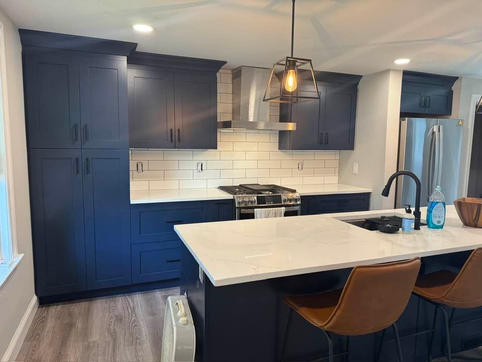 Modern kitchen with navy blue cabinets, white countertops, and a kitchen island with brown bar stools.