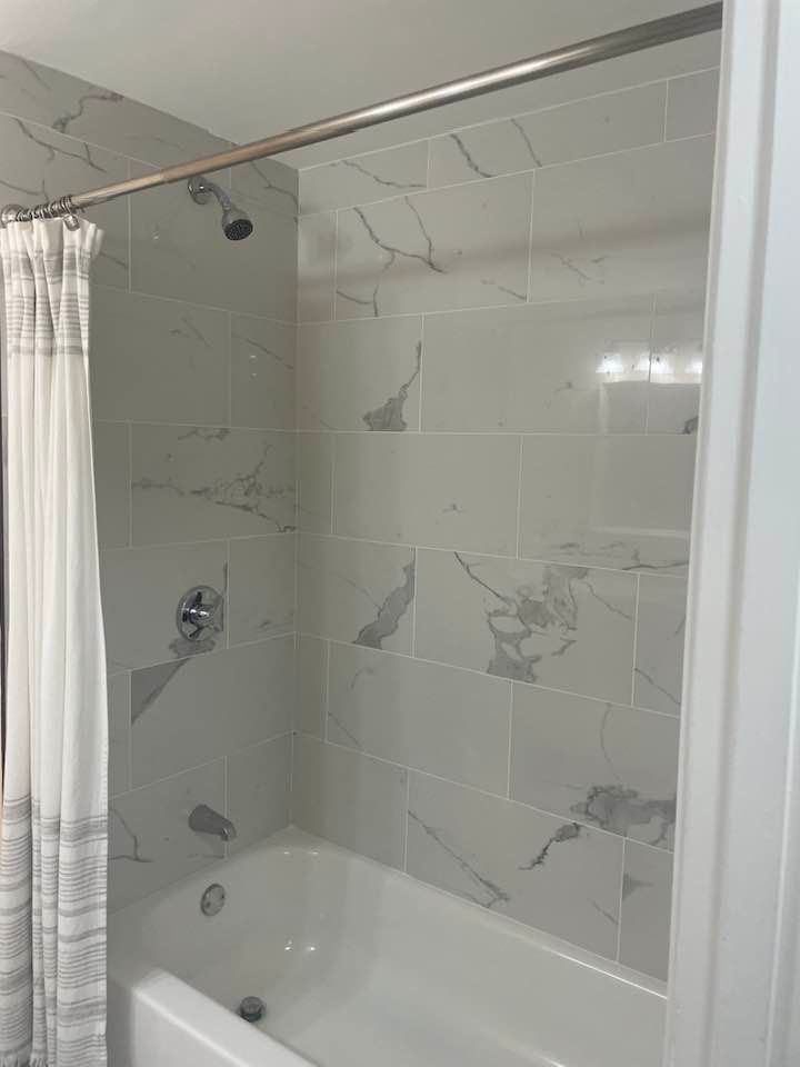 Bathroom with marble-like tile walls, shower curtain, and tub. Chrome showerhead and fixtures.