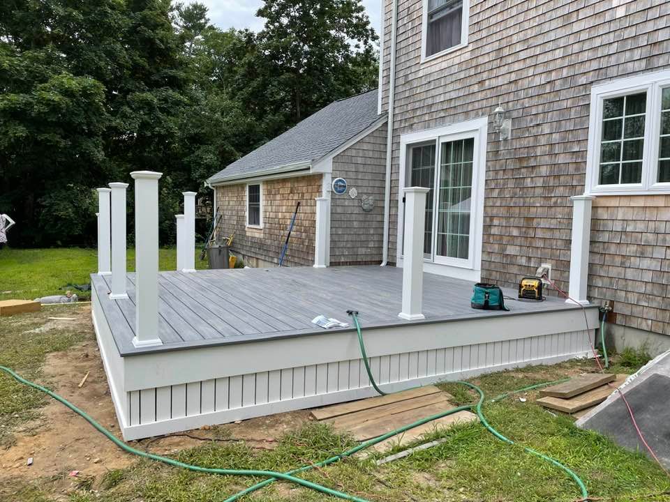 A newly constructed gray deck with white railing and skirt attached to a gray shingled house.