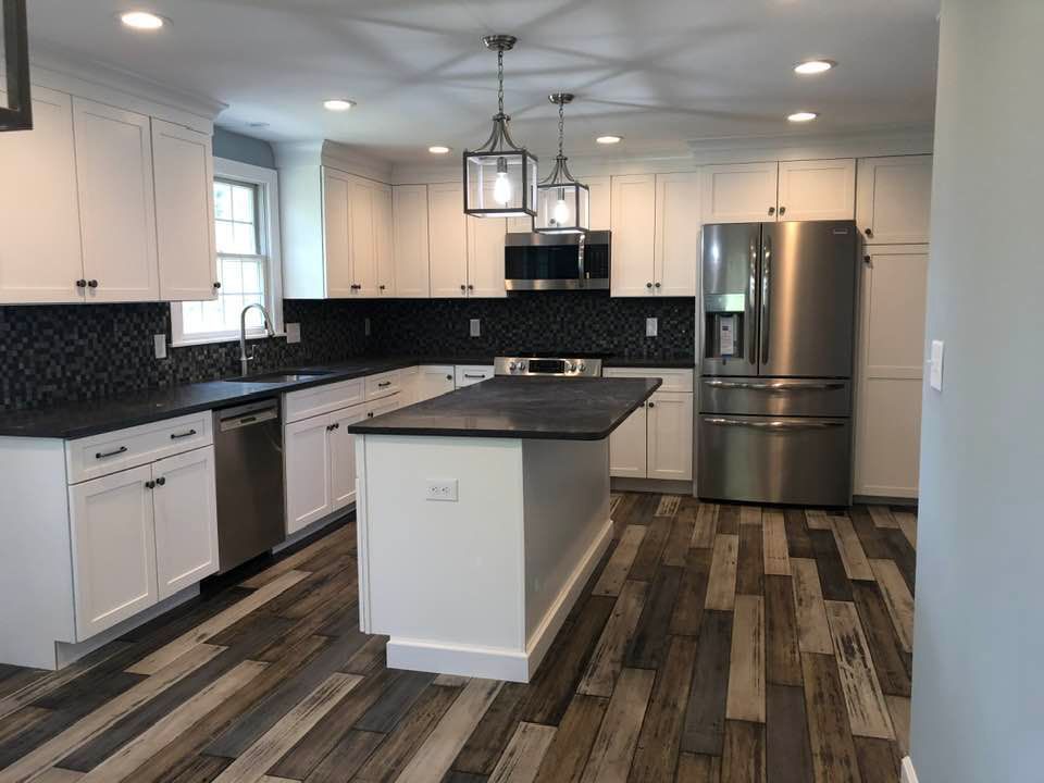 White kitchen with stainless steel appliances, black countertops, and patterned wood floor.